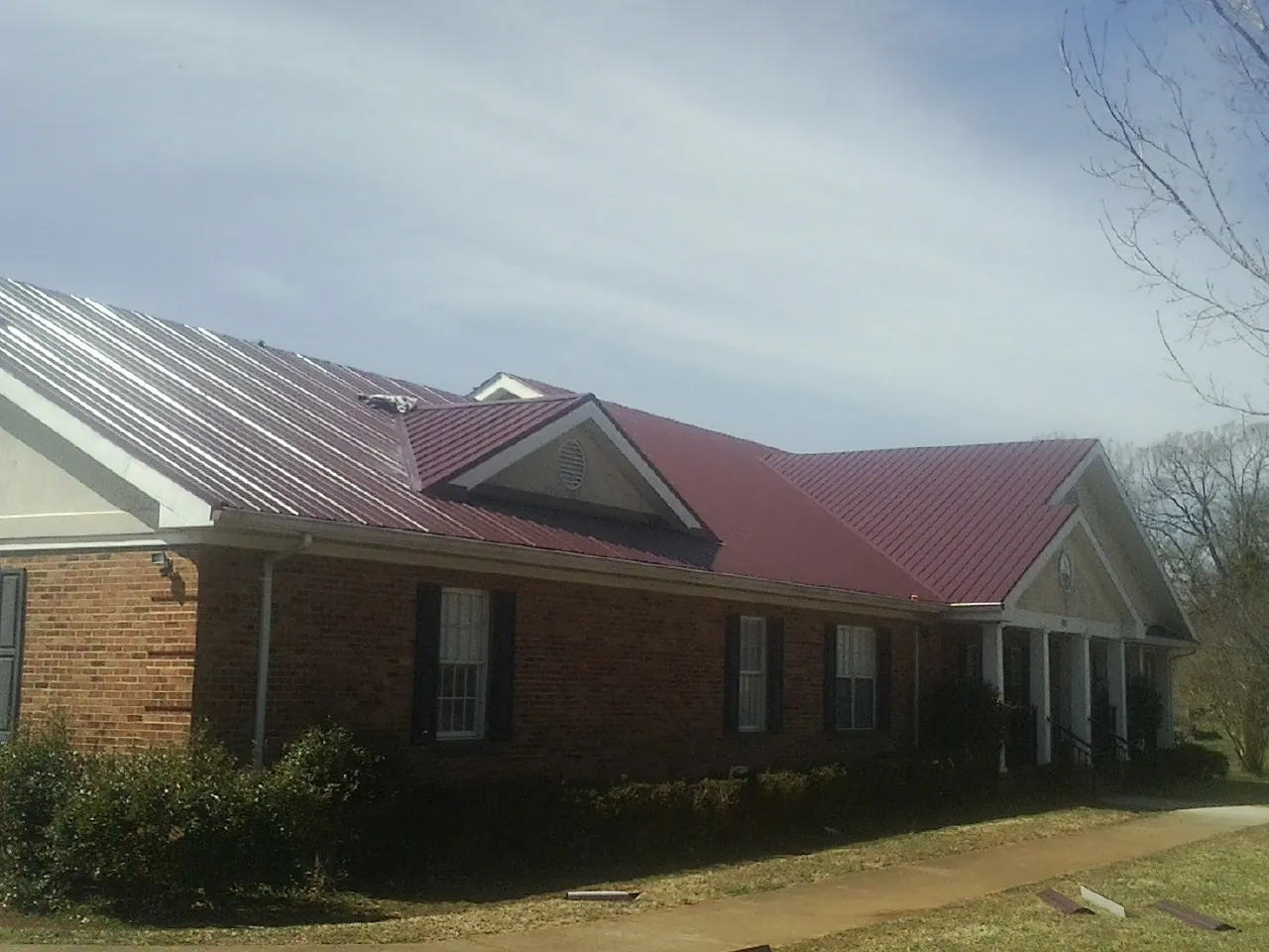 Red metal roof with gabled entries on a long brick building, from a Hail Damage Roof Repair job in Toddville