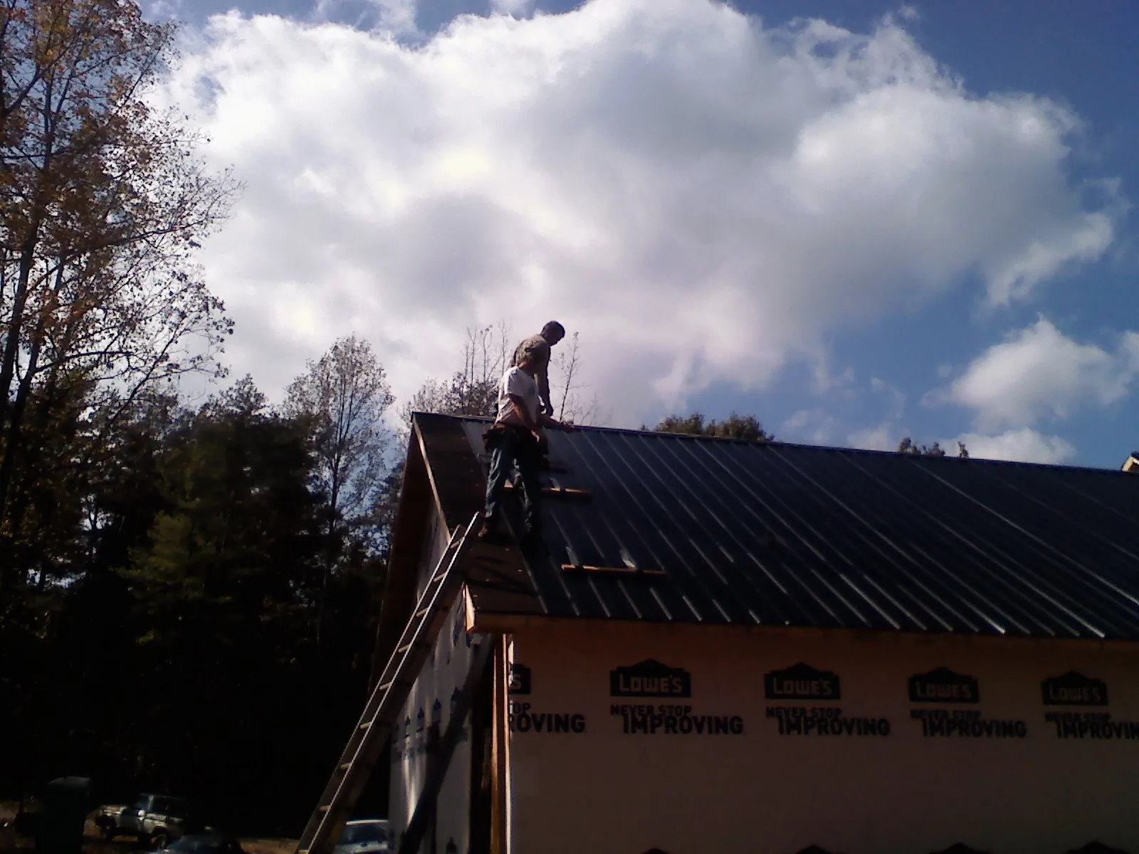 Roofer fastening dark metal panels high against a cloudy sky, from a Roof Inspection job in Toddville