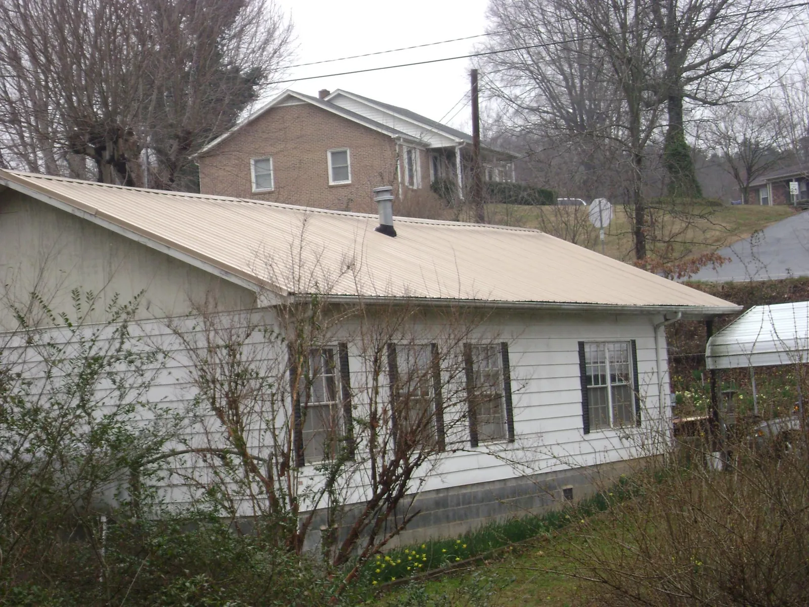 Tan metal roof on a white sided house set into a hillside — Commercial Roofing by Roofing Brothers in Toddville