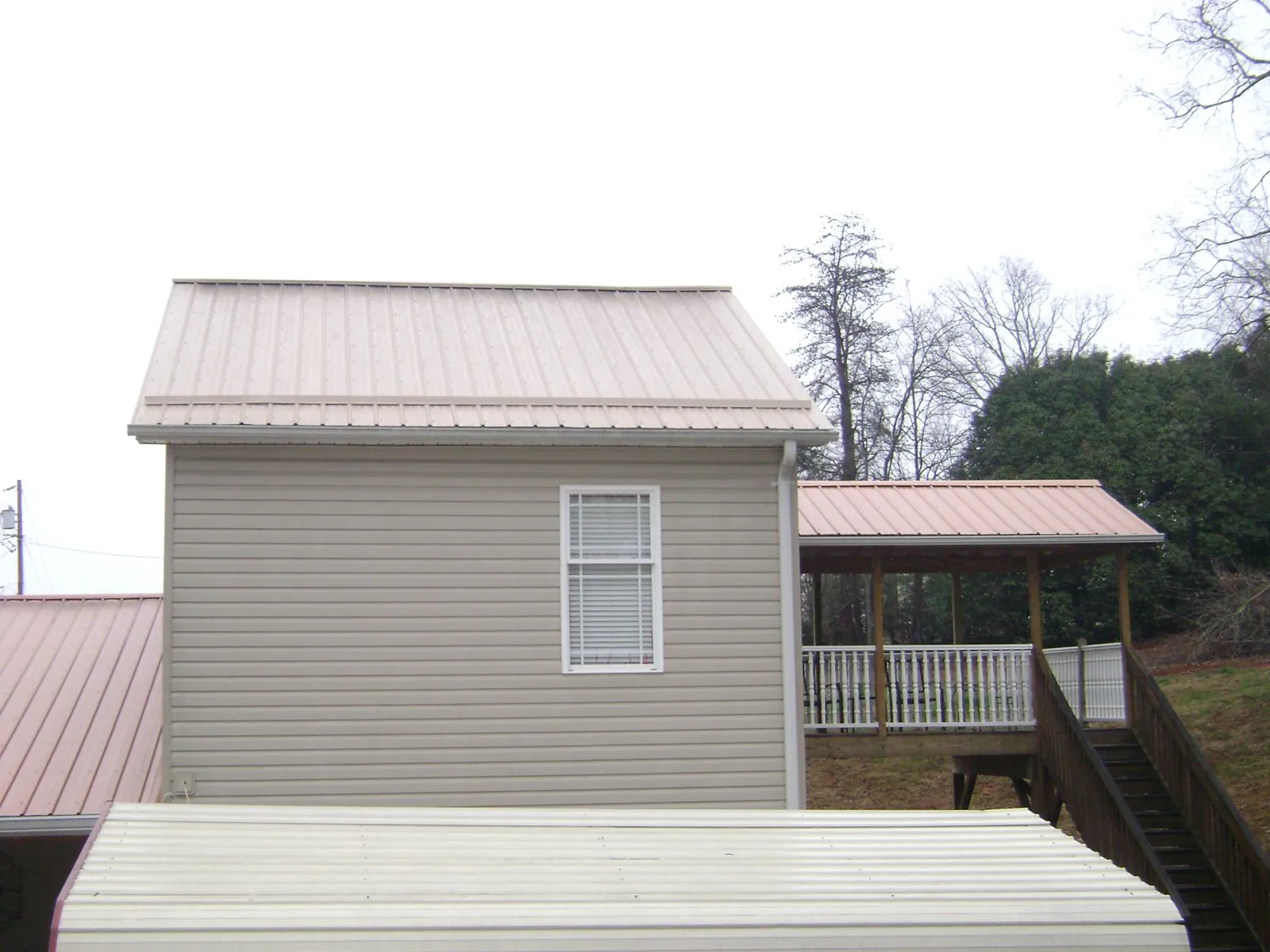 Tan metal roofs on a two story addition and attached porch, from a Roof Replacement job in Toddville